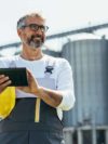 Ingenieur vor verschwommenen Getreidesilos arbeitet an Tablet mit Enterprise Asset Management