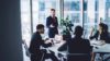 Geschäftsmann im formellen schwarzen Anzug, der neben seinen Kollegen steht und einen Finanzbericht während einer Konferenz in einem modernen Arbeitsraum analysiert und über die Implementierung der SAP Sales Cloud redet